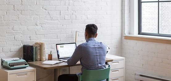Mann sitzt am Schreibtisch, vorm Laptop, mit Blick zur Wand.