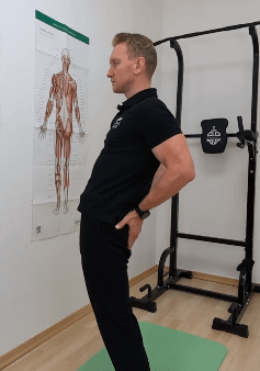 Denny steht aufrecht, hat seine Hände auf dem Po und schiebt seine Leiste nach vorn.