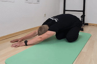 Denny ist im Kniestand. Der Por liegt auf den Fersen, der Oberkörper ist nach seitlich vorn abgelegt. (Child-Position)