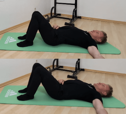 Beckenkippen liegend: Denny liegt in Rückenlage auf dem Boden und kippt sein Becken nach vorn (unterer Rücken wölbt sich vom Boden weg), dann kippt er es nach hinten (unterer Rücken liegt komplett auf dem Boden).