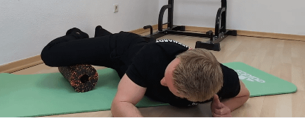 Denny liegt in Bauchlage. Sein rechtes Bein ist seitlich angewinkelt. Die Oberschenkelinnenseite liegt auf einer Faszienrolle.