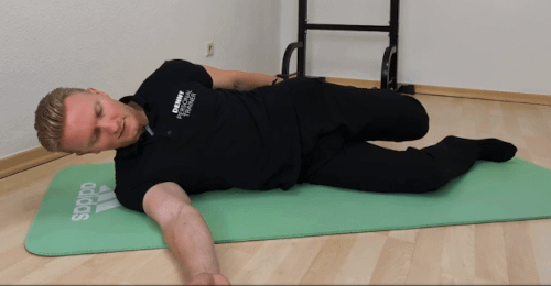 Hohlkreuz Frau: Denny liegt in Seitenlage und hält seinen Fuß, vom oberen Bein, hinten am Po.