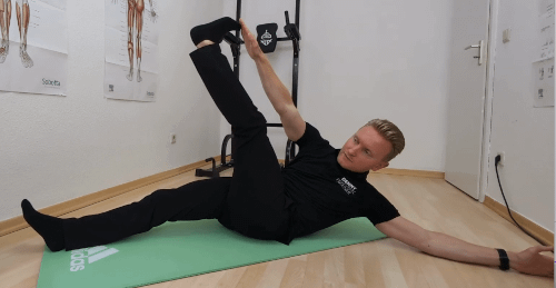 Hohlkreuz Frau Bauch (Dead Bug): Denny liegt in Rückenlage. Sein rechter Arm und das diagonale Bein sind zueinander nach oben gestreckt.